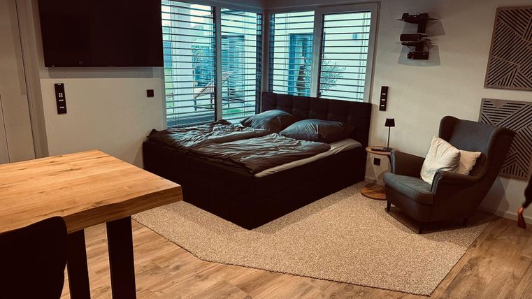 Ein modernes Schlafzimmer mit einem Doppelbett und großen Fenstern. Der Bereich ist hell und freundlich, mit Holz- und Teppichboden.