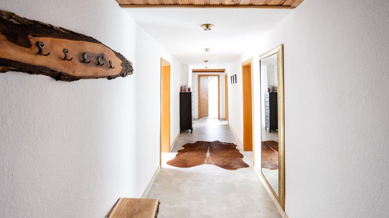 Ein heller Flur mit weißer Wandfarbe und Holzdetails. An der Wand hängen Haken, und ein großer Spiegel ist ebenfalls vorhanden.