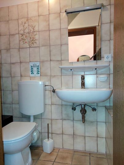 Ein kleines Badezimmer mit einer Toilette, einem Waschbecken und einem Spiegel. Die Wände sind mit hellen Fliesen dekoriert.