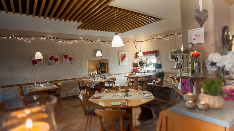 Ein gemütliches Restaurant mit Holzmöbeln und warmem Licht. Die Wände sind mit Kunstwerken und Pflanzen dekoriert, was eine einladende Atmosphäre schafft.