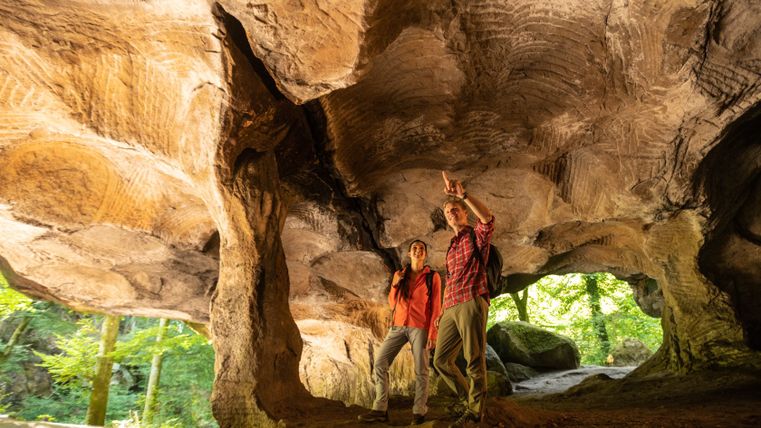 Zwei Wanderer stehen in einer Felsenhöhle mit gewölbter Decke und schauen nach oben.