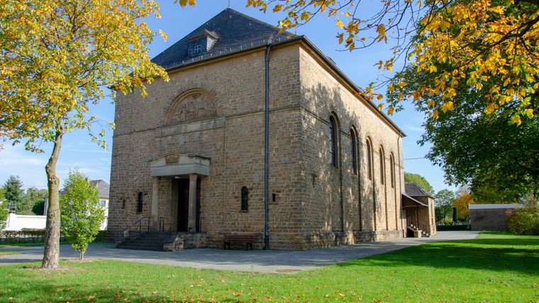 Kirche St. Hubertus in Wolsfeld, umgeben von Bäumen im Herbst.