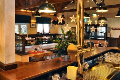 Ein gemütliches Restaurant mit Holzdekor und einer einladenden Bar. Die Tische sind schön gedeckt und Pflanzen sorgen für eine angenehme Atmosphäre.