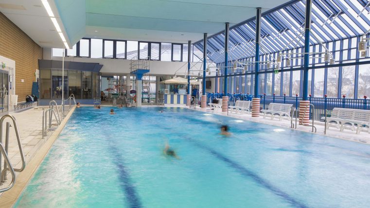 Ein Schwimmbad mit klarem Wasser und modernen Einrichtungen. Große Fenster lassen viel Licht herein und schaffen eine einladende Atmosphäre.