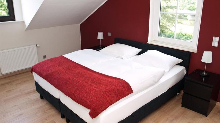 Ein modernes Schlafzimmer mit einem großen Bett und roten Wänden. Neben dem Bett stehen zwei Nachtkommoden mit Lampen.