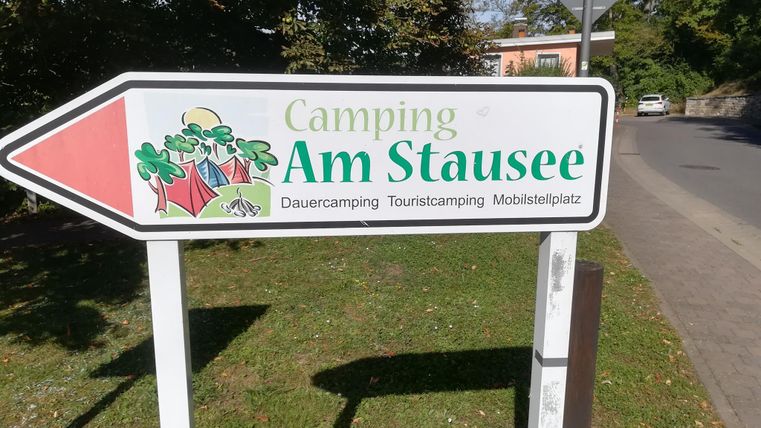 Ein Schild zeigt den Weg zum Campingplatz "Am Stausee". Der Platz bietet Dauer- und Touristen-Camping sowie Mobilstellplätze.