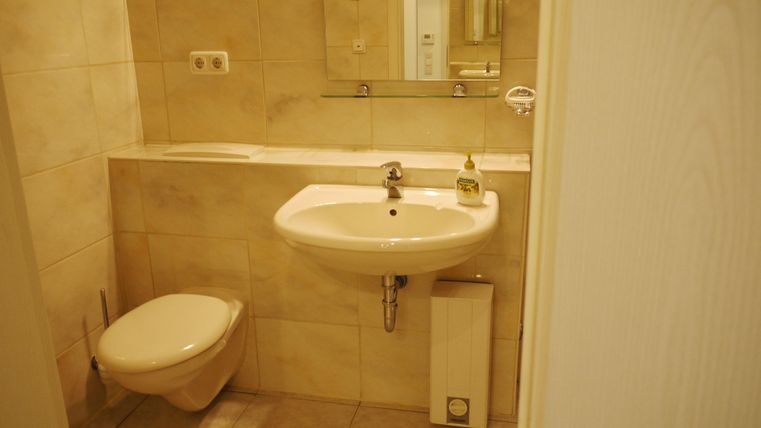 Ein modernes Badezimmer mit einem Waschbecken und einer Toilette. Die Wände sind hell gefliest und es gibt einen Spiegel über dem Waschbecken.