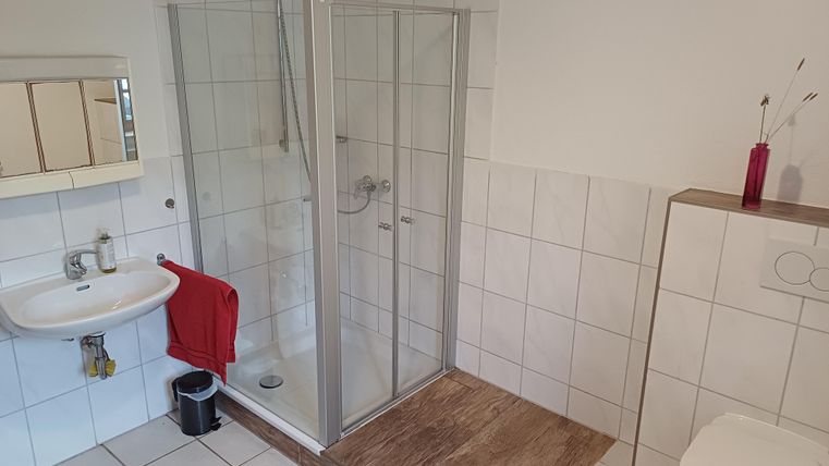 Ein modernes Badezimmer mit einer Dusche und einem Waschbecken. Weiße Fliesen und ein Holzbelag sorgen für ein einladendes Ambiente.