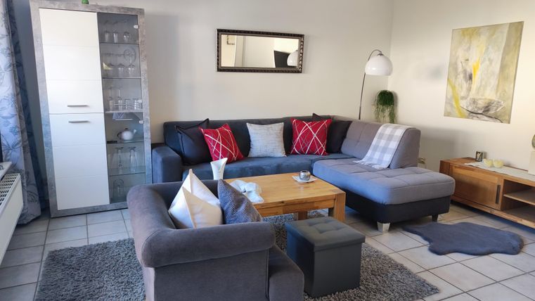 Ein gemütliches Wohnzimmer mit einem großen, grauen Sofa und bunten Kissen. Der Raum hat einen modernen Look mit Holzmöbeln und Kunst an der Wand.