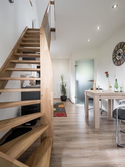 Eine moderne Treppe aus Holz führt in einen hellen Raum. Im Vordergrund steht ein Tisch mit einigen Pflanzen und Getränken.
