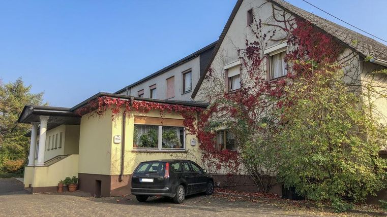 Ein Gebäude mit einer gelben Fassade, das teilweise von Pflanzen überwuchert ist. Vor dem Haus steht ein schwarzes Auto.