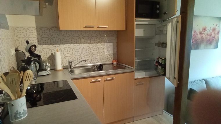 Eine moderne Küche mit Holzschränken und Edelstahlgeräten. Der Kühlschrank ist offen und es gibt eine gemütliche Sitzgelegenheit im Hintergrund.