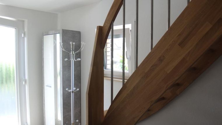 Ein heller Eingangsbereich mit einer modernen Treppe aus Holz. Ein Garderobenständer und ein Schrank ergänzen den Raum.