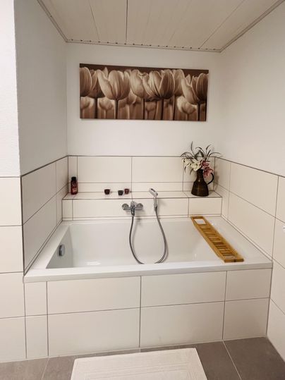 Ein modernes Badezimmer mit einer großen Badewanne und eleganter Fliesenwand. An der Wand hängt ein dekoratives Bild von Tulpen.
