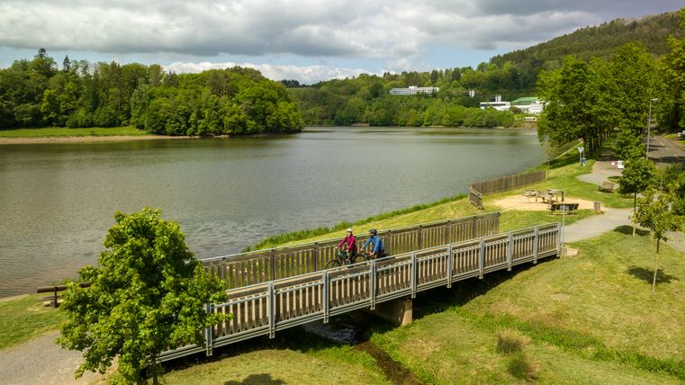 Zwei Fahrradfahrer auf einer Brücke über einen Nebenfluss vor dem Stausee