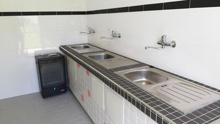 Eine moderne Küche mit mehreren Spülen und einem kleinen Kühlschrank. Die Wände sind einfach weiß gefliest.