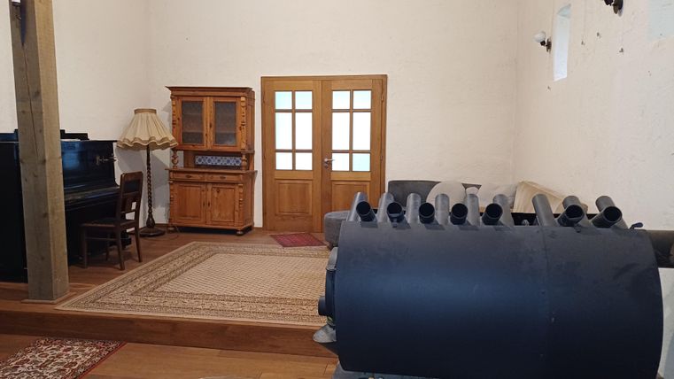 Ein gemütlicher Raum mit einem Klavier und einem Holzschrank. Im Vordergrund ist ein schwarzes Objekt zu sehen.