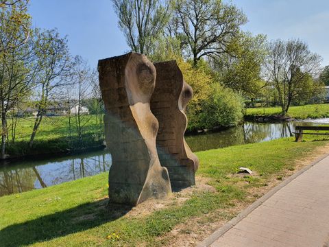 Stone sculpture on the riverbank with trees in the background.