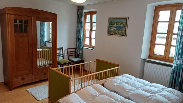 Ein gemütliches Schlafzimmer mit einem Doppelbett und einem Babybett. Der Raum hat große Fenster und einen klassischen Schrank aus Holz.