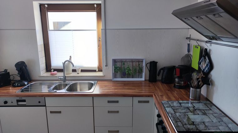 Eine moderne Küche mit Holzarbeitsplatte und klaren Linien. Das Fenster lässt viel Licht herein und zeigt eine Pflanze im Fensterbrett.