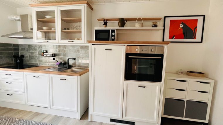 Eine moderne Küche mit weißen Schränken und Holzakzenten. Sie ist gut ausgestattet mit einem Herd, einer Mikrowelle und einem Kühlschrank.