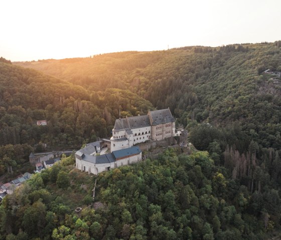 Aerial view of Vianden Castle in Luxembourg at sunset. The castle sits majestically on a hill surrounded by dense forests., &copy; lft_cpcreatives
