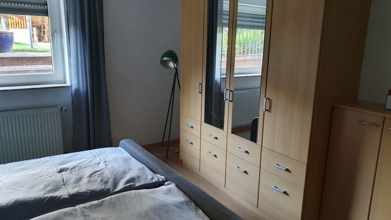 Ein gemütliches Schlafzimmer mit einem Bett, einem Kleiderschrank und einer stehlampe. Das Fenster lässt viel Tageslicht hereinfällen.